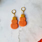 close up of Triple stack pumpkin earrings on a marble background with fall foliage.