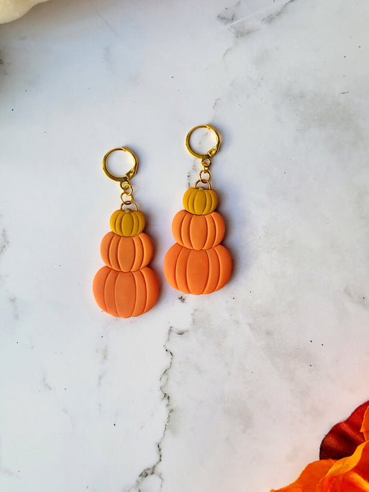 close up of Triple stack pumpkin earrings on a marble background with fall foliage.
