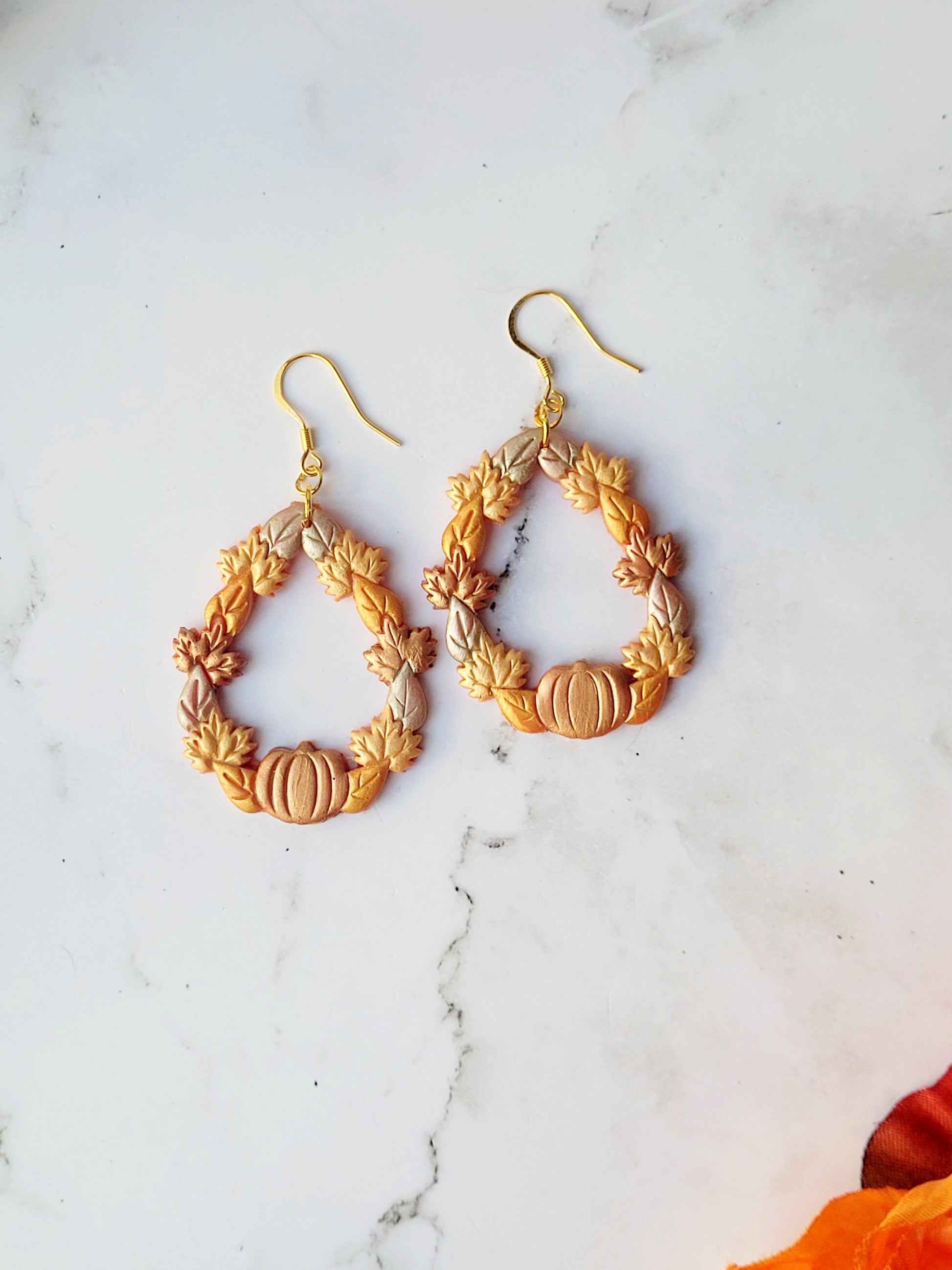 close up of fall harvest themed teardrop earrings on a marble background