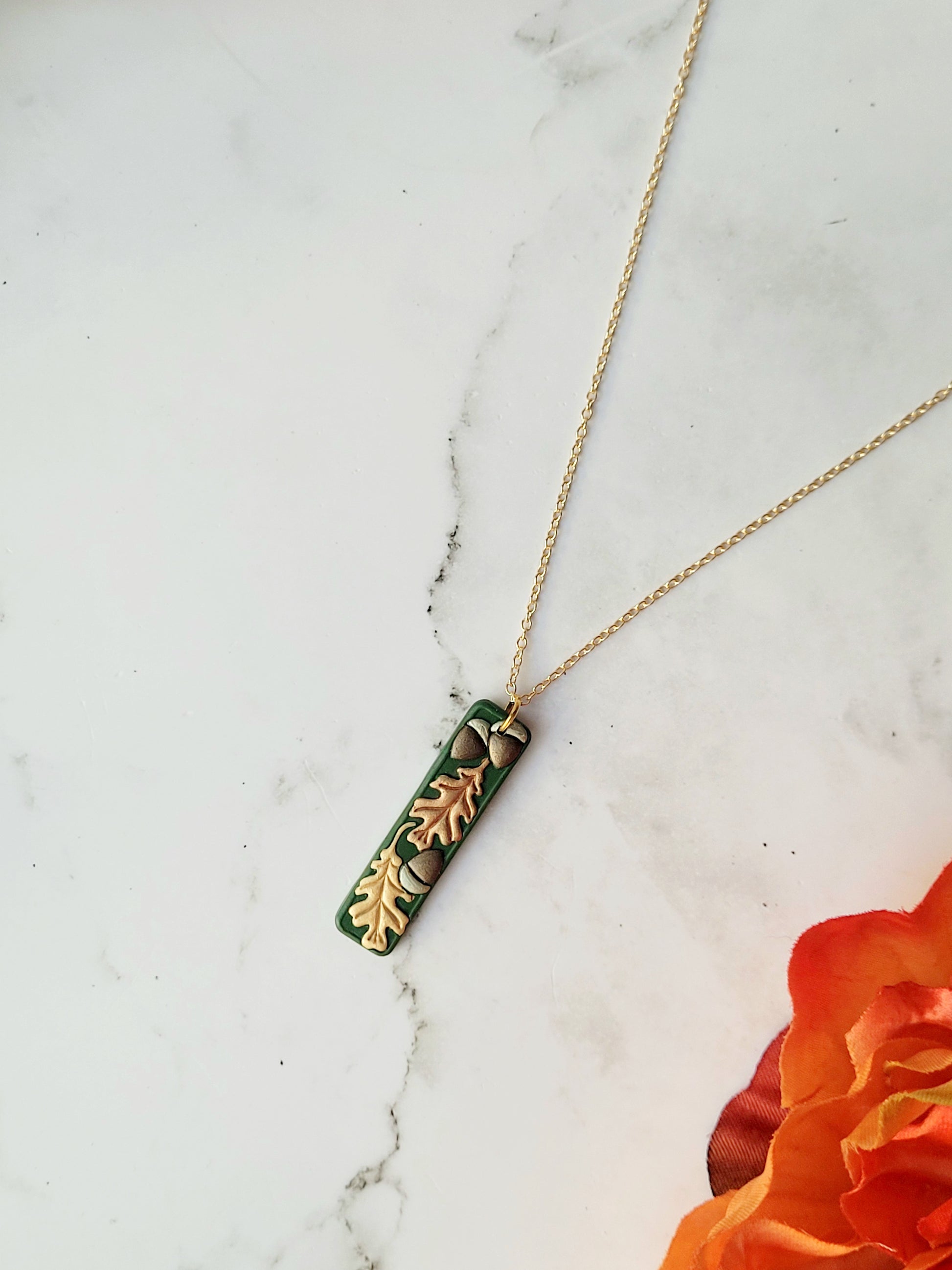 close up of the Green bar shaped pendant with metallic acorns and oak leaves.