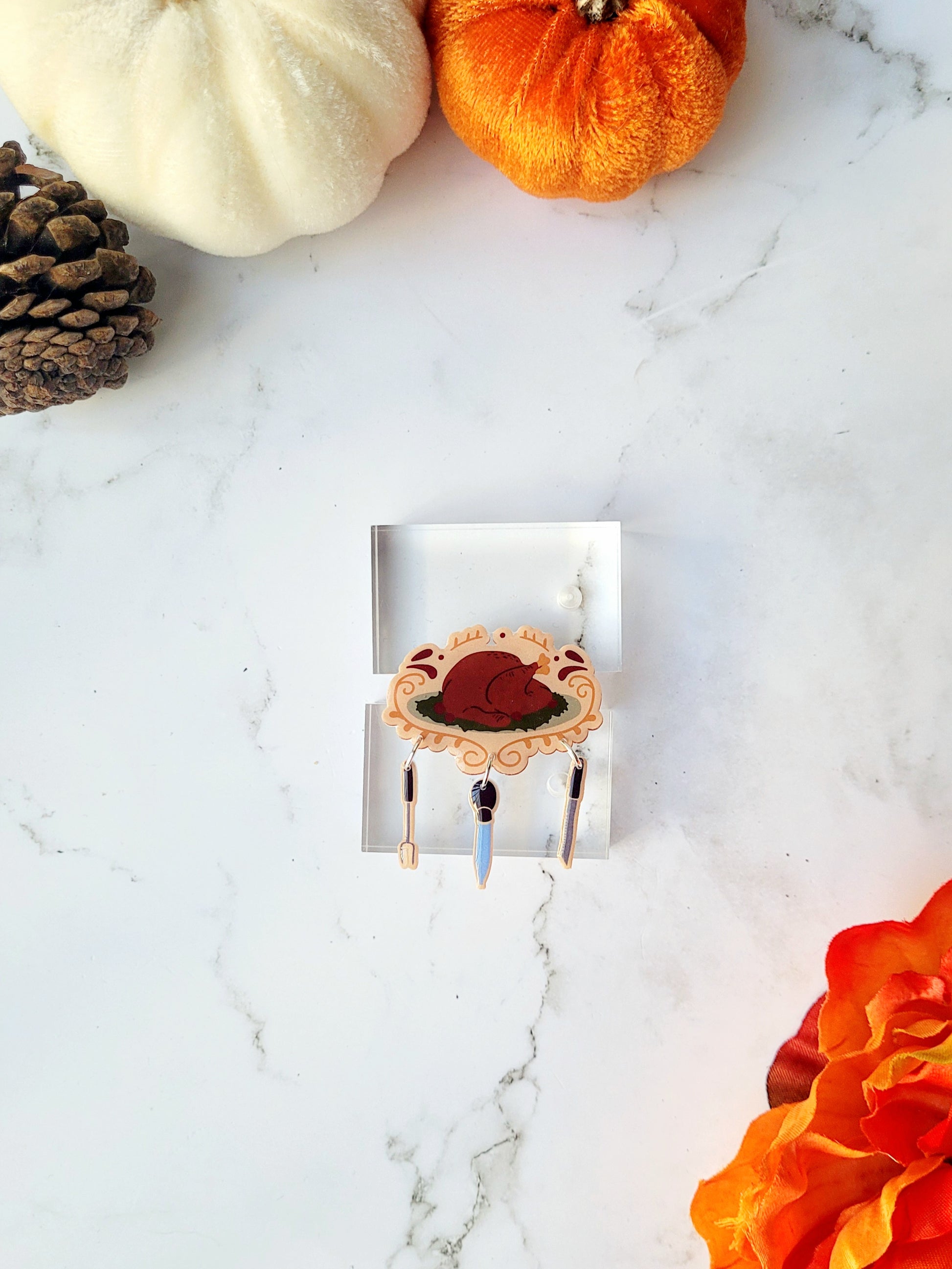 cooked turkey with utensil charm brooch on a marble background with fall foliage. 