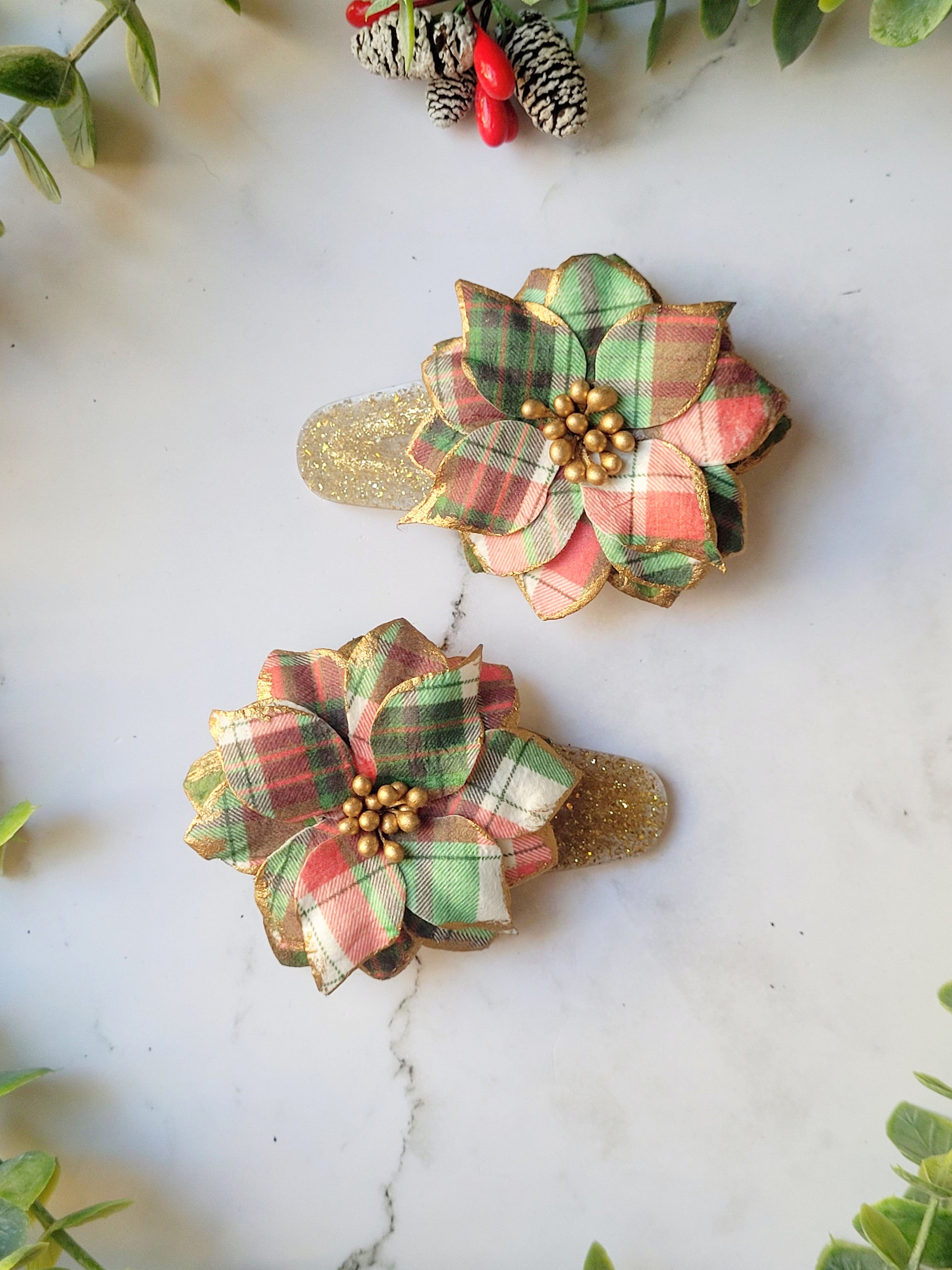 close up of the Christmas themed plaid poinsettia hair clip  on a marble background surrounded by foliage.