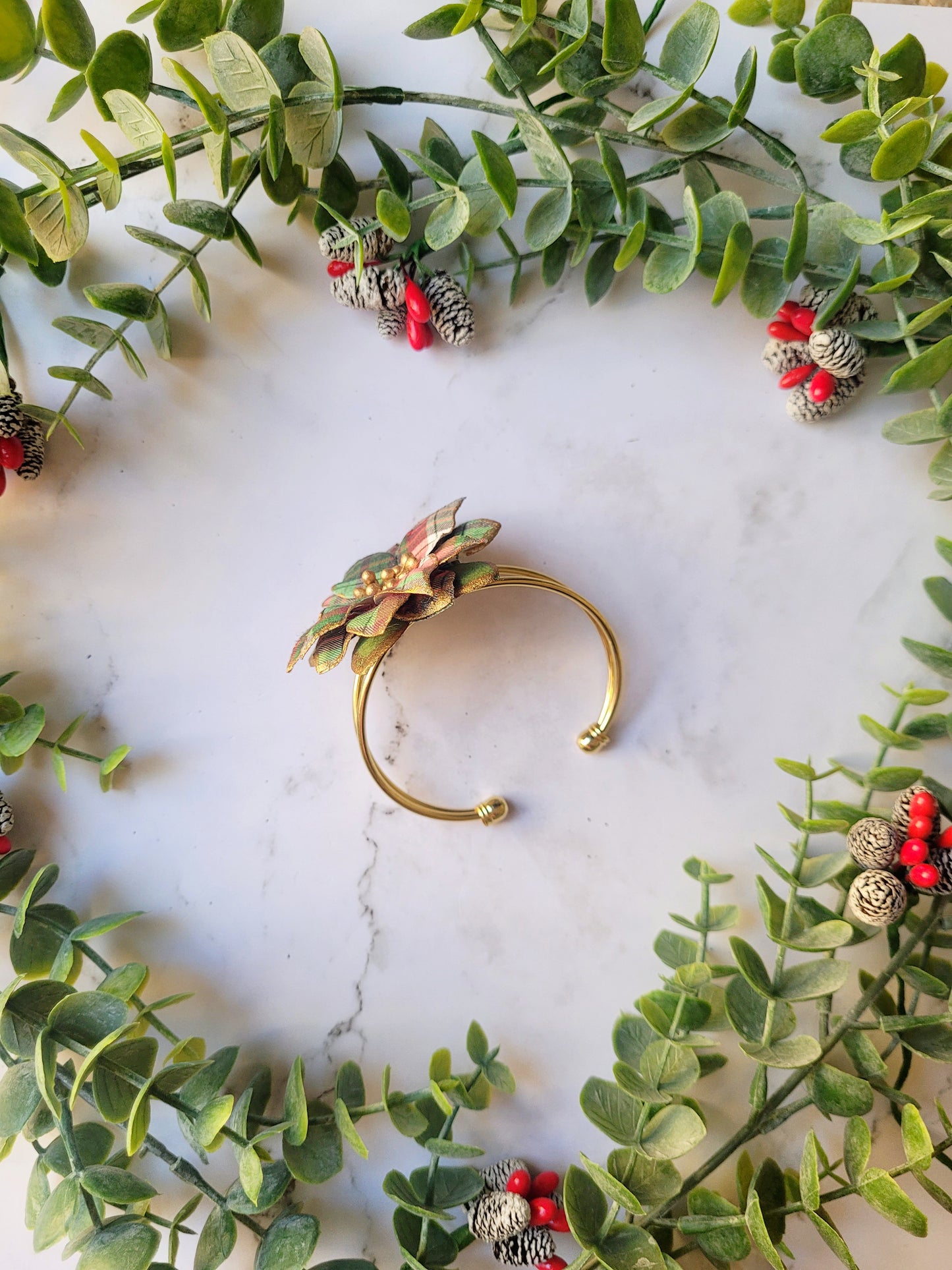 side view of the Christmas themed plaid poinsettia bracelet on a marble background surrounded by foliage.