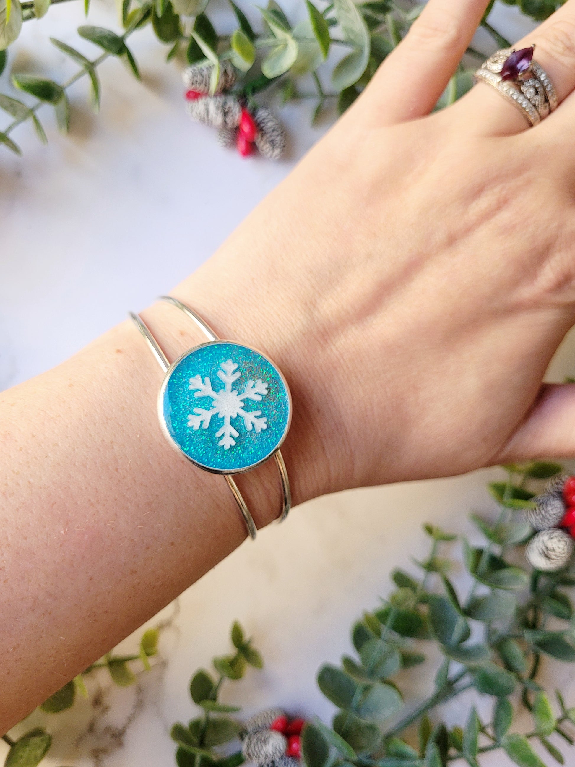 close up of silver braceclet with a blue glitter charm and a white snowflake on wrist for size reference 