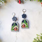 painted winter landscape earrings on a marble background with foliage. 