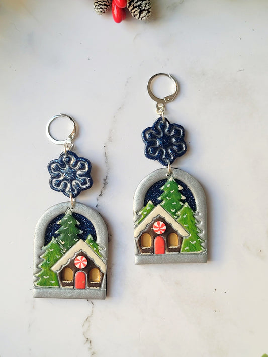 close up of painted winter landscape earrings on a marble background with foliage. 