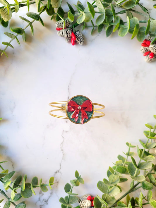 green and red bow bracelet on a marble background surrounded by foliage. 
