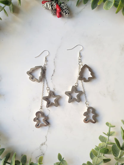 close up of Christmas cookie cutter dangle earrings in silver on a white marble background. .