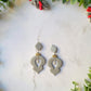 Silver glitter ornament shaped earrings with a pearl accent on a marble background with foliage. 