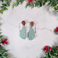 mint green tear drop earrings with a winter botanical print and wood studs on a marble background with foliage. 