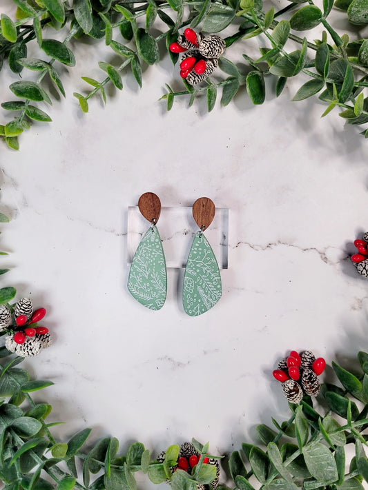 mint green tear drop earrings with a winter botanical print and wood studs on a marble background with foliage. 