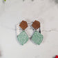 close up of mint green winter botanical earrings on a marble background surrounded by foliage.
