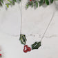 close up of Glitter holly sprig necklace on a marble background surrounded by foliage,
