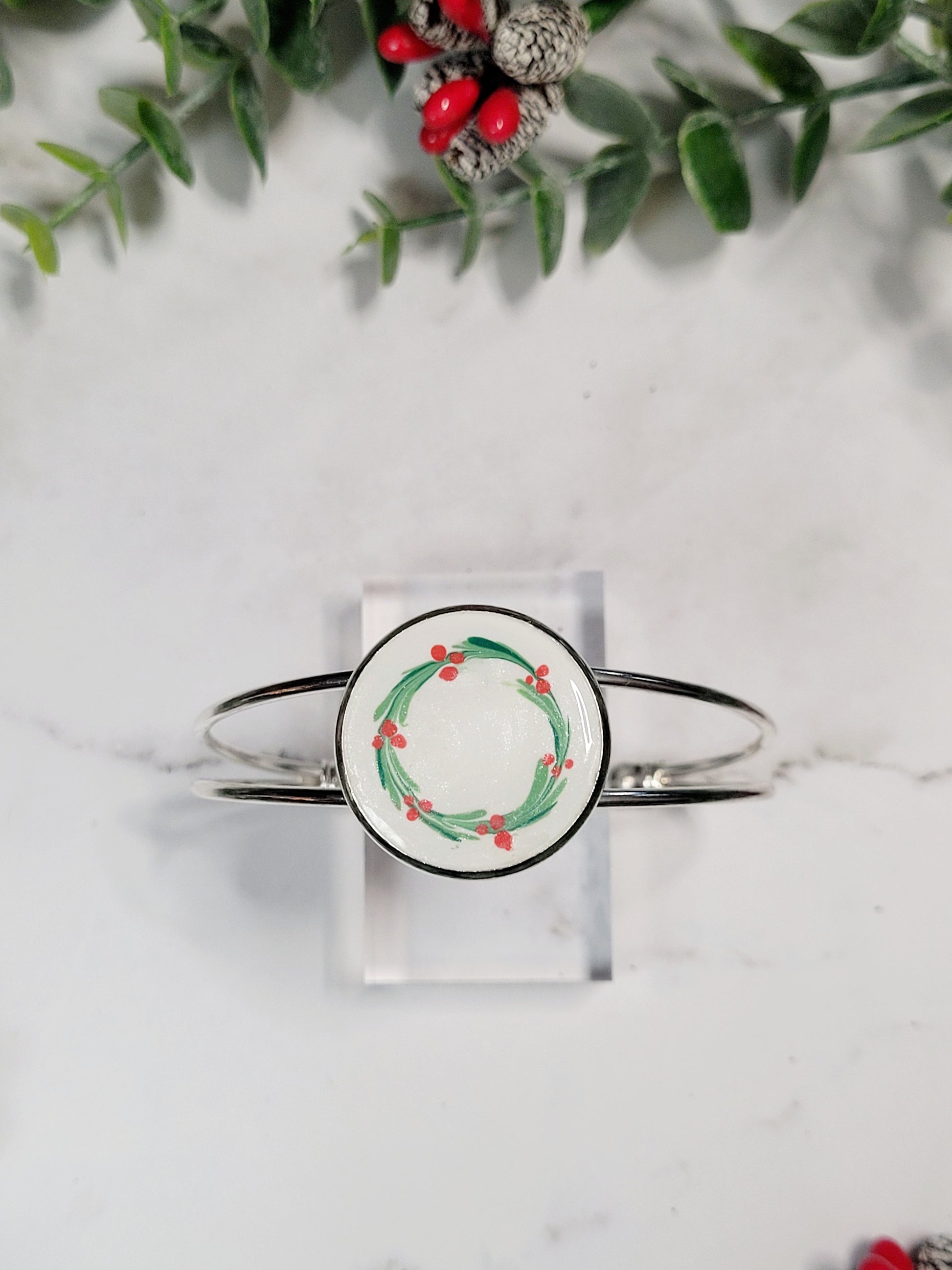 close up of silver mistletoe bracelet on a marble background surrounded by foliage.