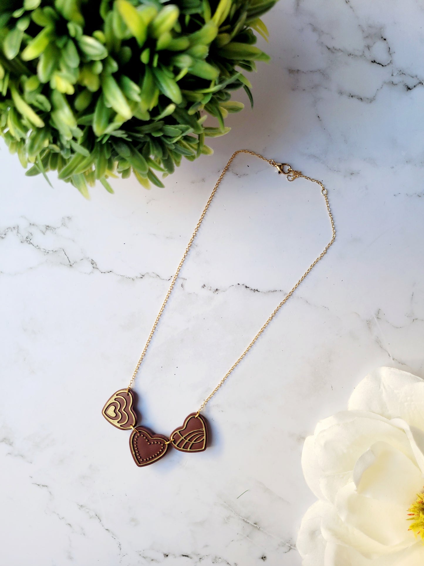 Chocolate and gold heart truffle necklace on a white background.