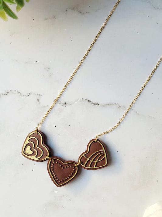 close up of Chocolate and gold heart truffle necklace on a white background.
