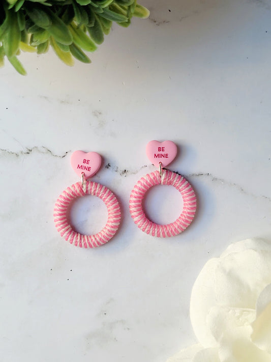 close up of pink and white striped hoops with a pink candy heart stud on a marble background with foliage