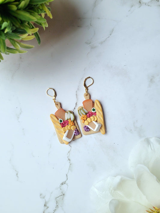 charcuterie board earrings on a white marble background. 
