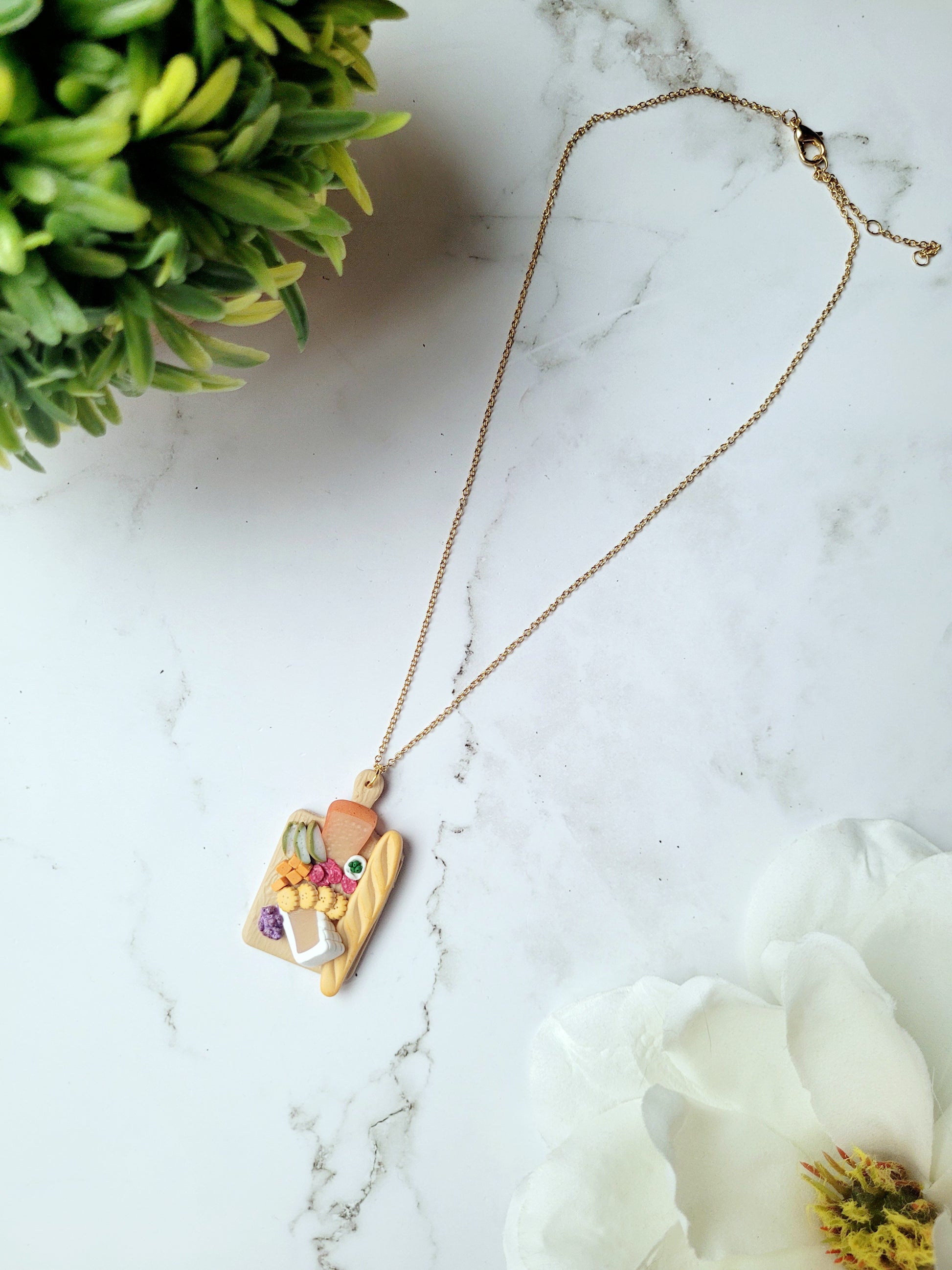 Charcuterie board necklace on a white marble background. 