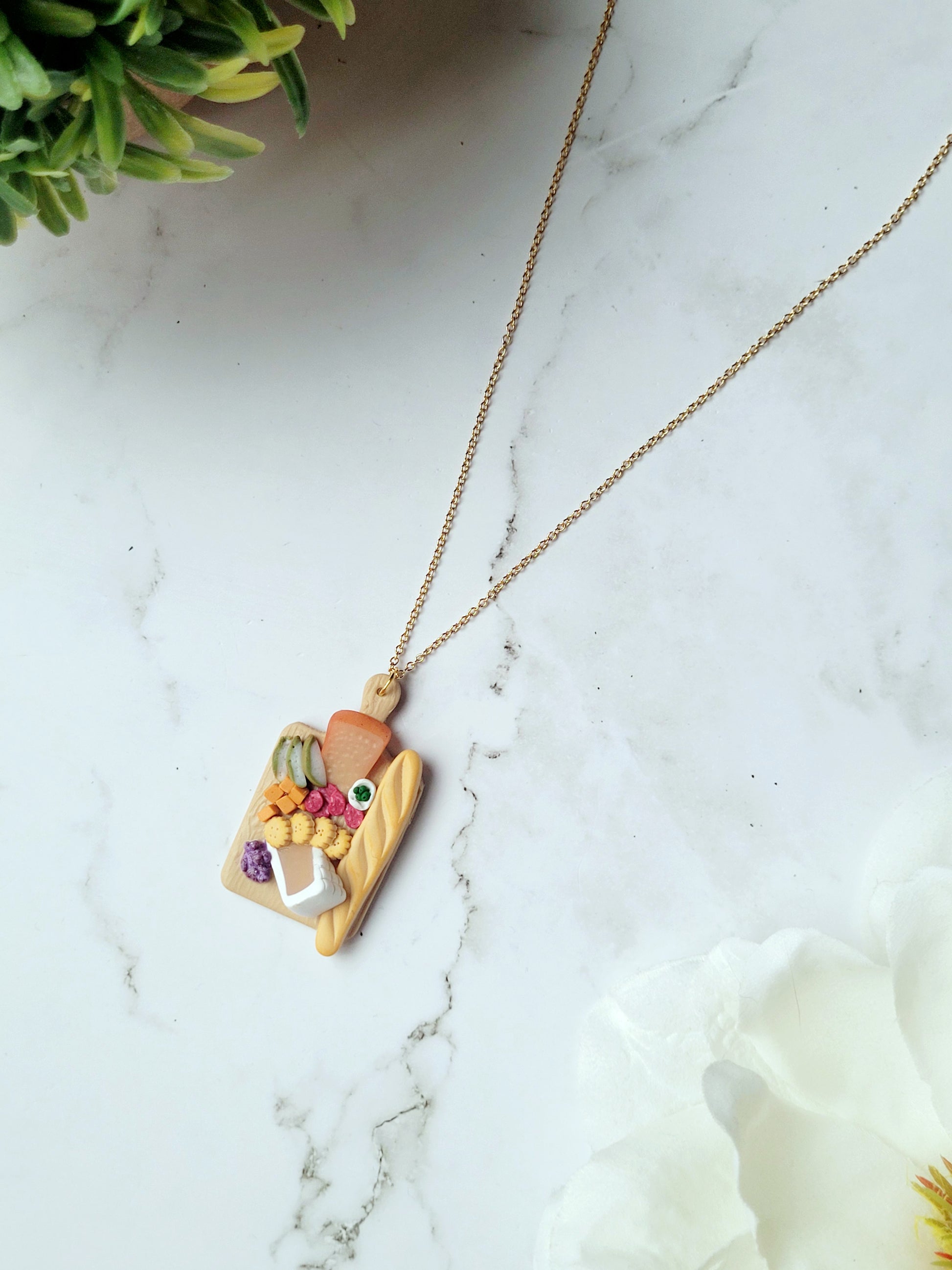 close up of Charcuterie board necklace on a white marble background.
