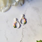 white teardrop hoops with painted tulips on a marble background with foliage. 