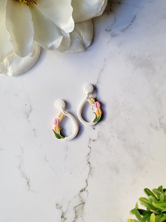 white teardrop hoops with painted tulips on a marble background with foliage. 