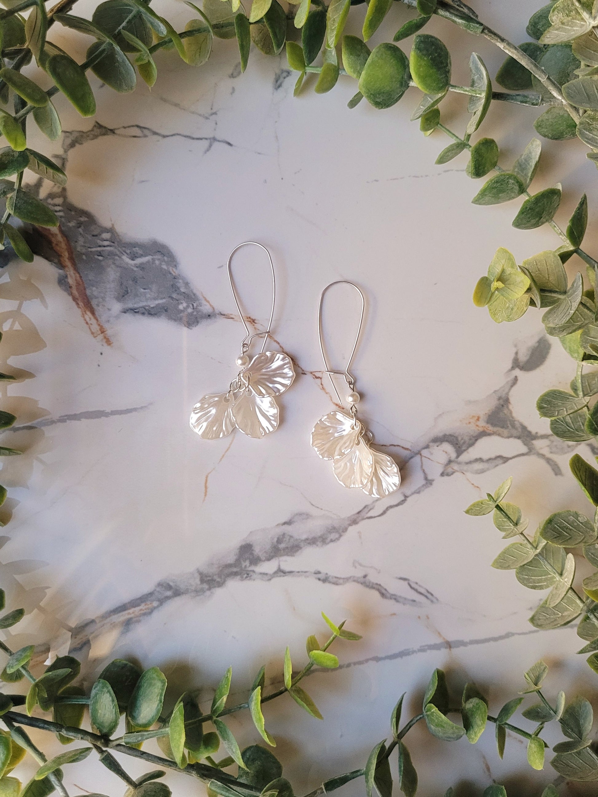 pearl petal dangle earrings on a marble background and foliage. 