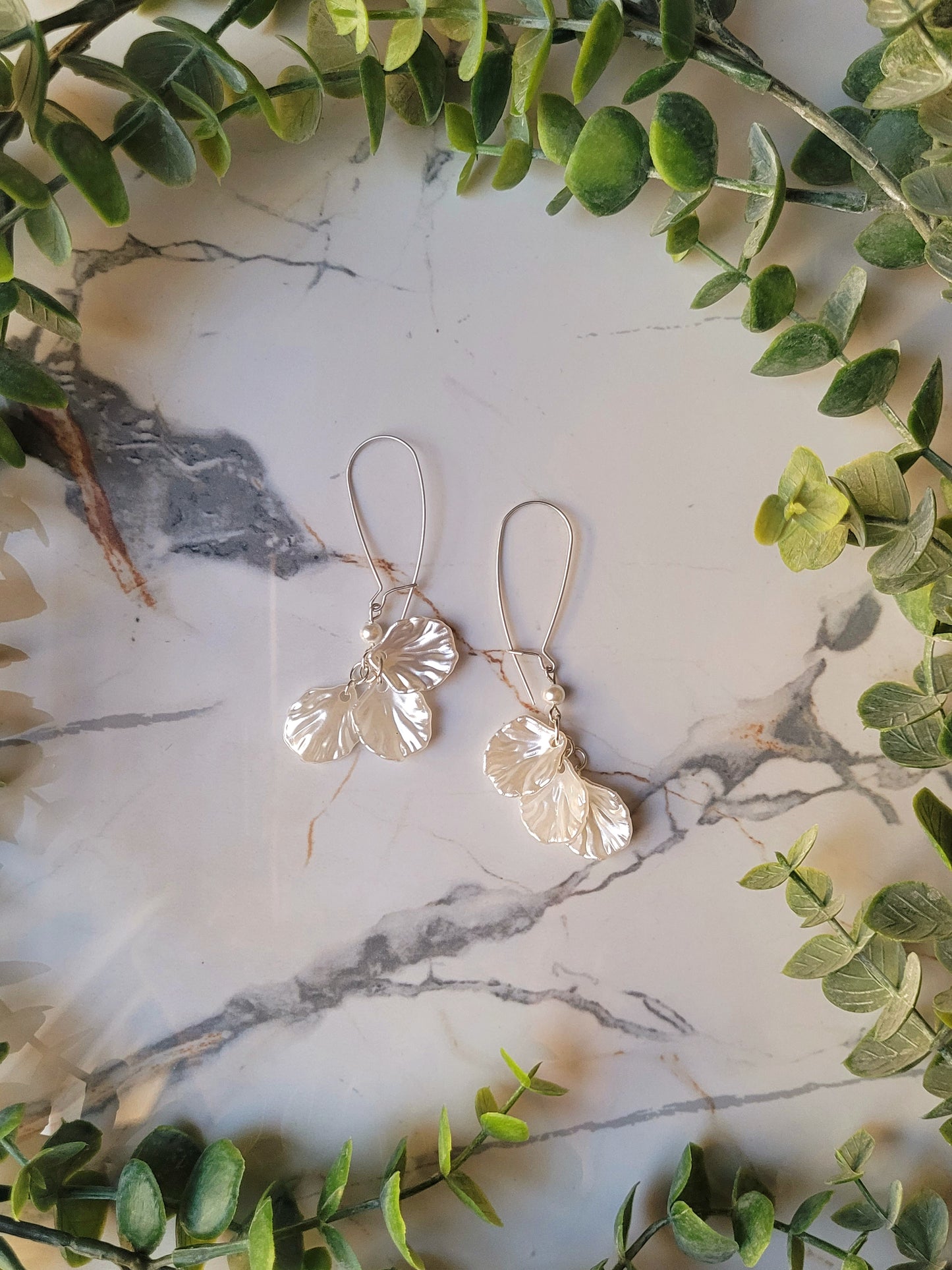 close up of pearl petal dangle earrings on a marble background and foliage.