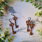 two shapes of skeleton key earrings with filigree in antique gold on a marble background with foliage. 