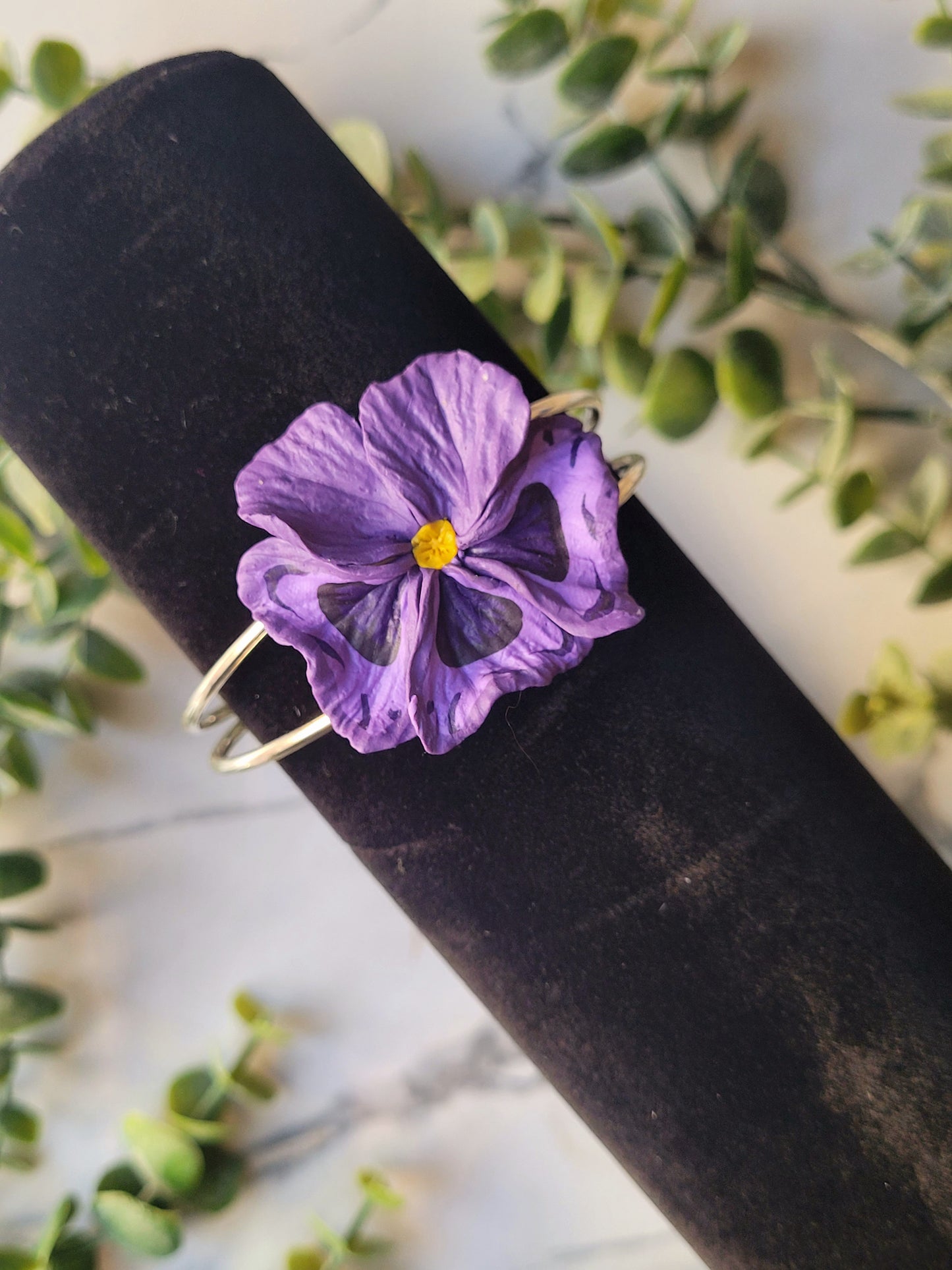 dark purple pansy flower bracelet on a black velvet holder.
