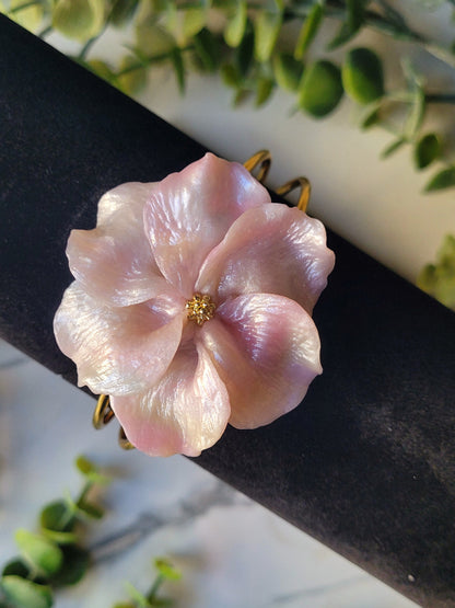 faux mother of pearl flower bracelet with gold findings on a marble background surrounded by foliage.