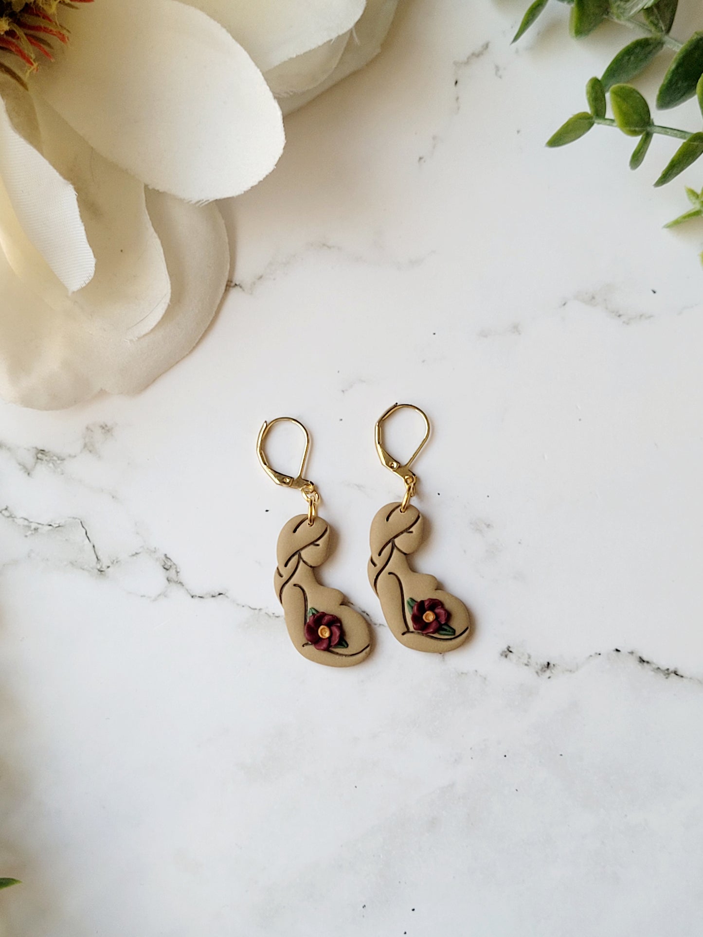 medium skin toned of pregnant women earrings on a marble background.