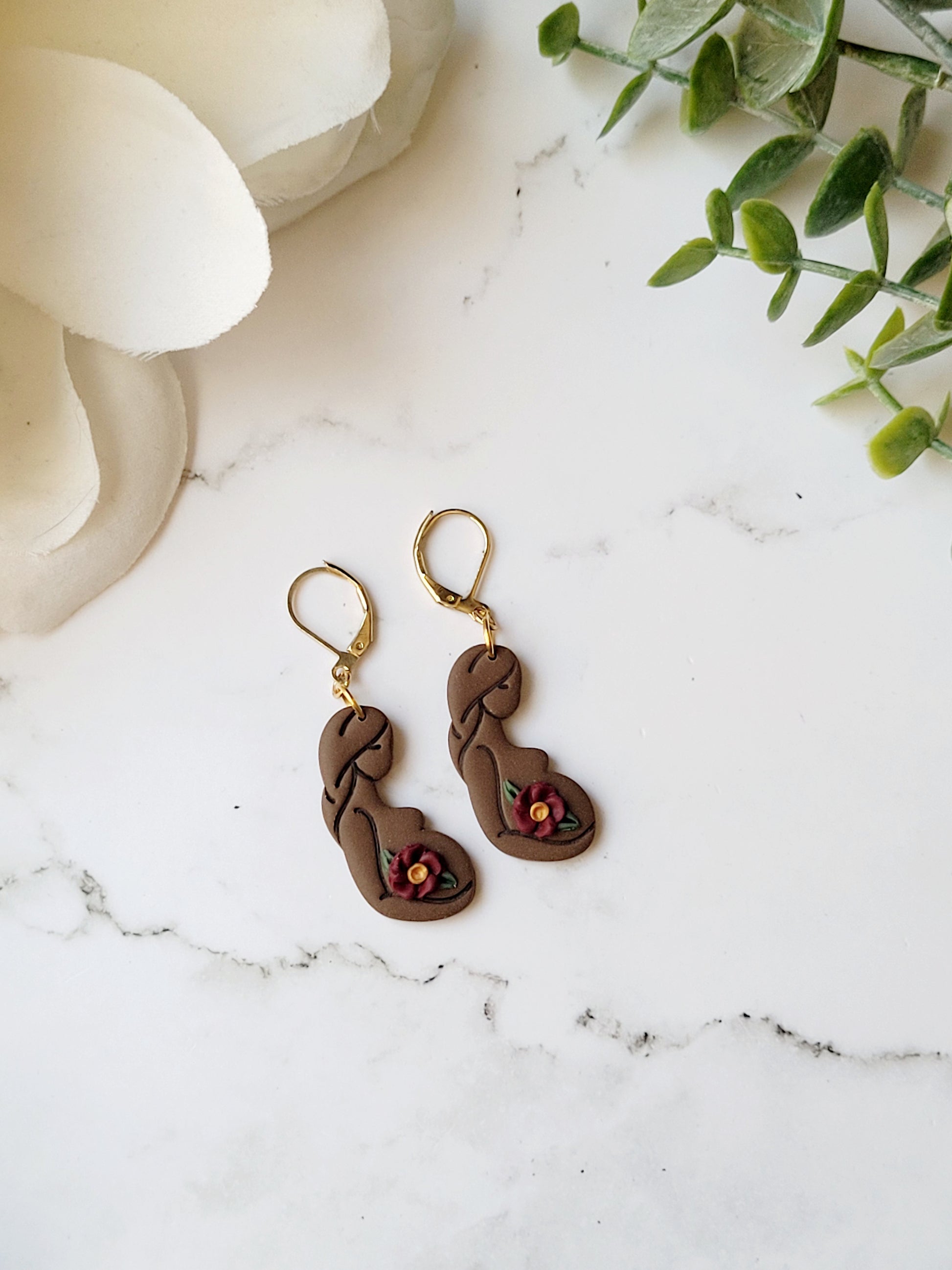 dark skin toned of pregnant women earrings on a marble background.