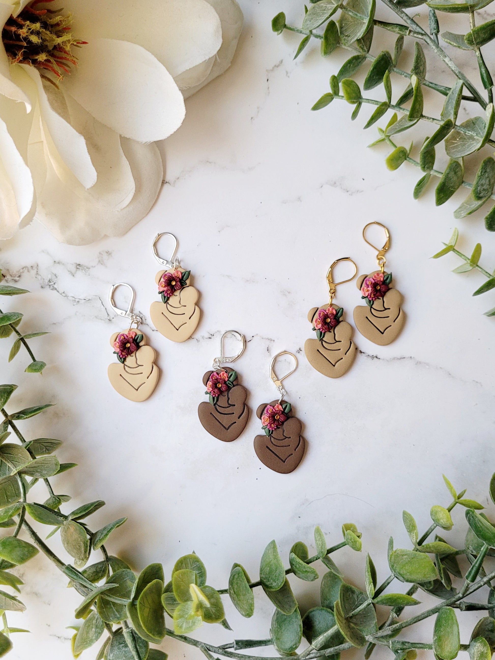 3 skin tones of mother with child earrings on a marble background.