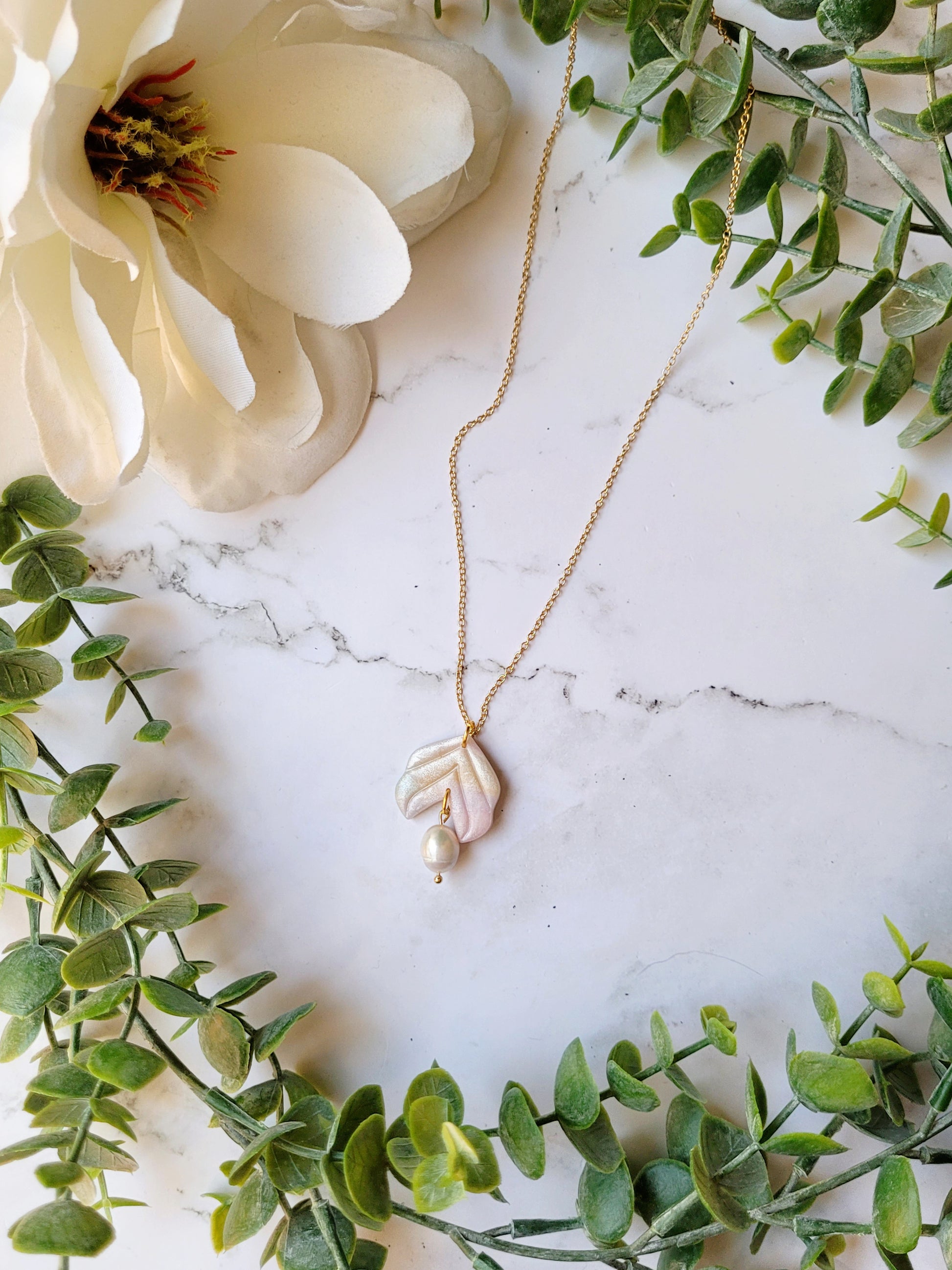 faux mother of pearl pendant with freshwater pearl accenton a marble background surrounded by foliage.