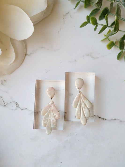 close up of faux mother of pearl clay earrings on a marble background surrounded by foliage.