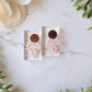 faux mother of pearl clay earrings on a marble background surrounded by foliage.