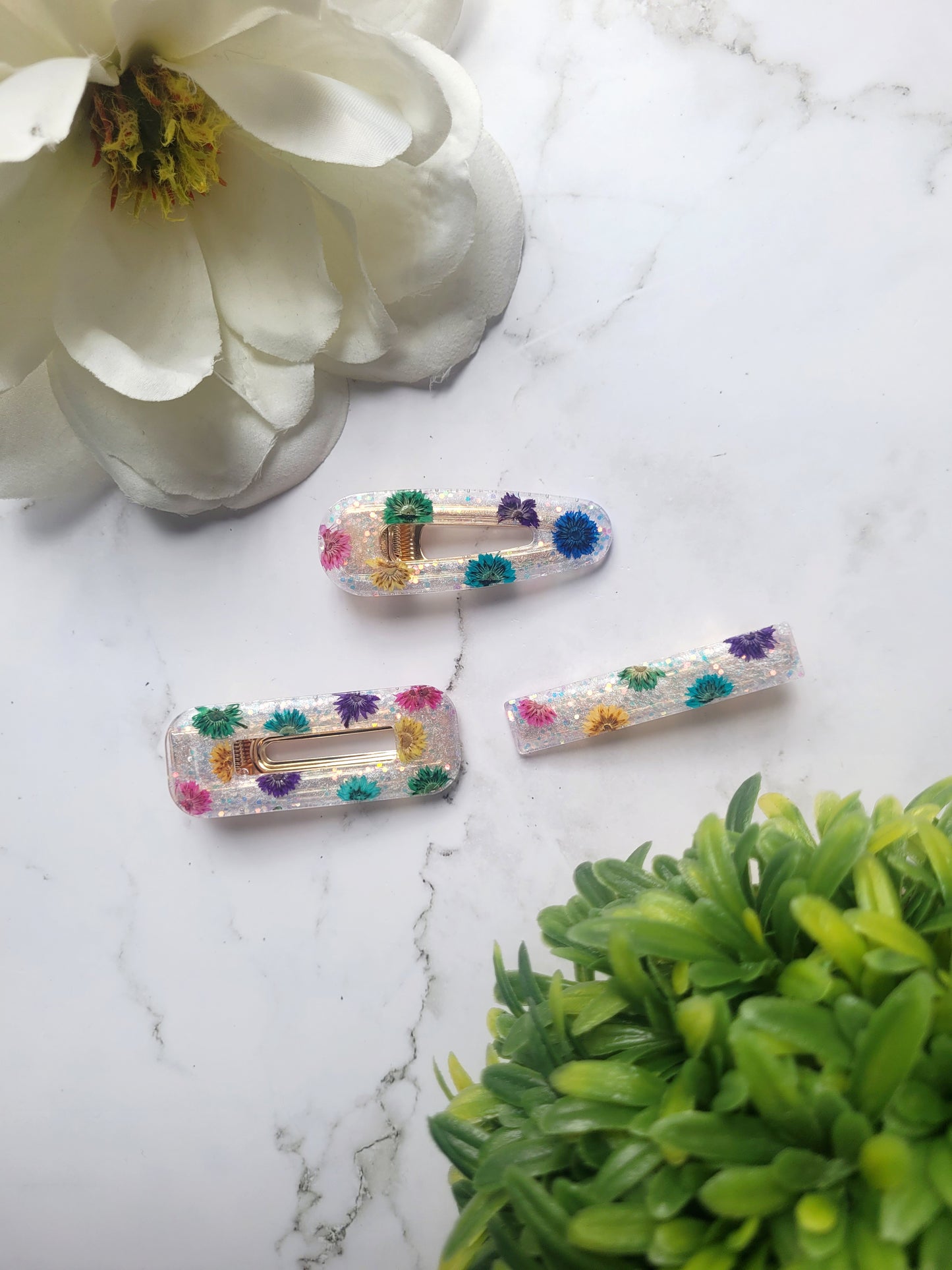 white glitter hair clips with rainbow dried flowers on a marble background. 