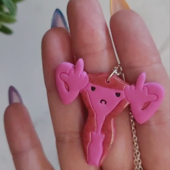 closeup of Pink uterus necklace with middle finger fallopian tubes. 