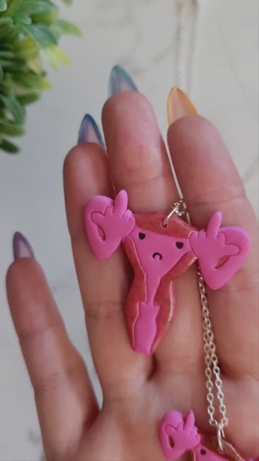 closeup of Pink uterus necklace with middle finger fallopian tubes. 