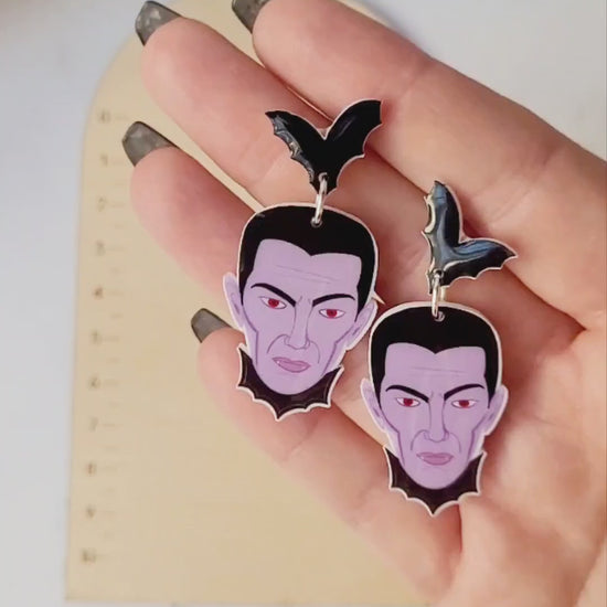 video close up of dracula dangle earrings on a white marble background with fall foliage.
