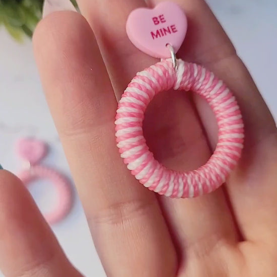 video close up of pink and white striped hoops with a pink candy heart stud on a marble background with foliage
