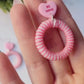 video close up of pink and white striped hoops with a pink candy heart stud on a marble background with foliage