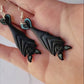 video close up of Black Hanging bat earrings on a white marble background .