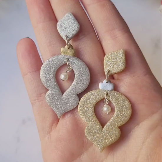video close up of Gold and Silver glitter ornament shaped earrings with a pearl accent on a marble background