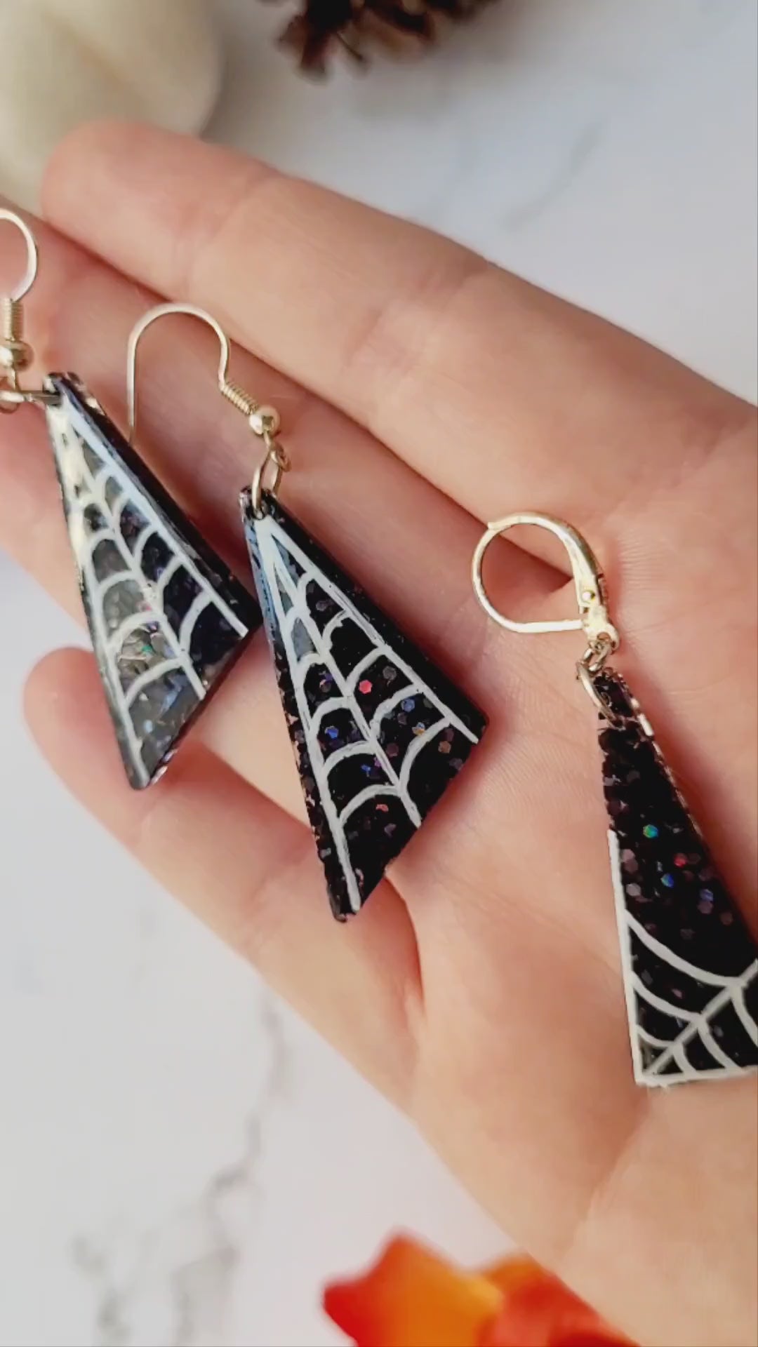 close up of black glitter earrings with white spider webs on ruler