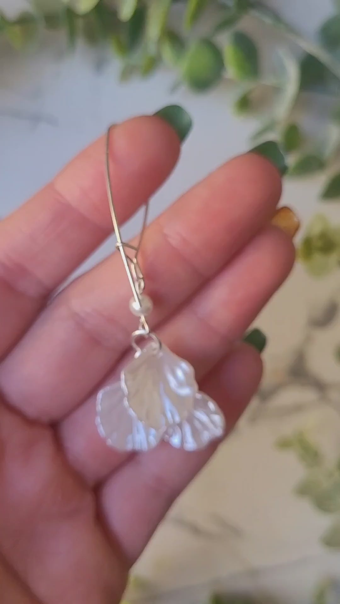 video close up of pearl petal dangle earrings on a marble background and foliage.