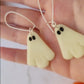 video close up of glow in the dark ghost earrings on a white marble background.