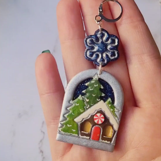 video close up of painted winter landscape earrings on a marble background with foliage. 