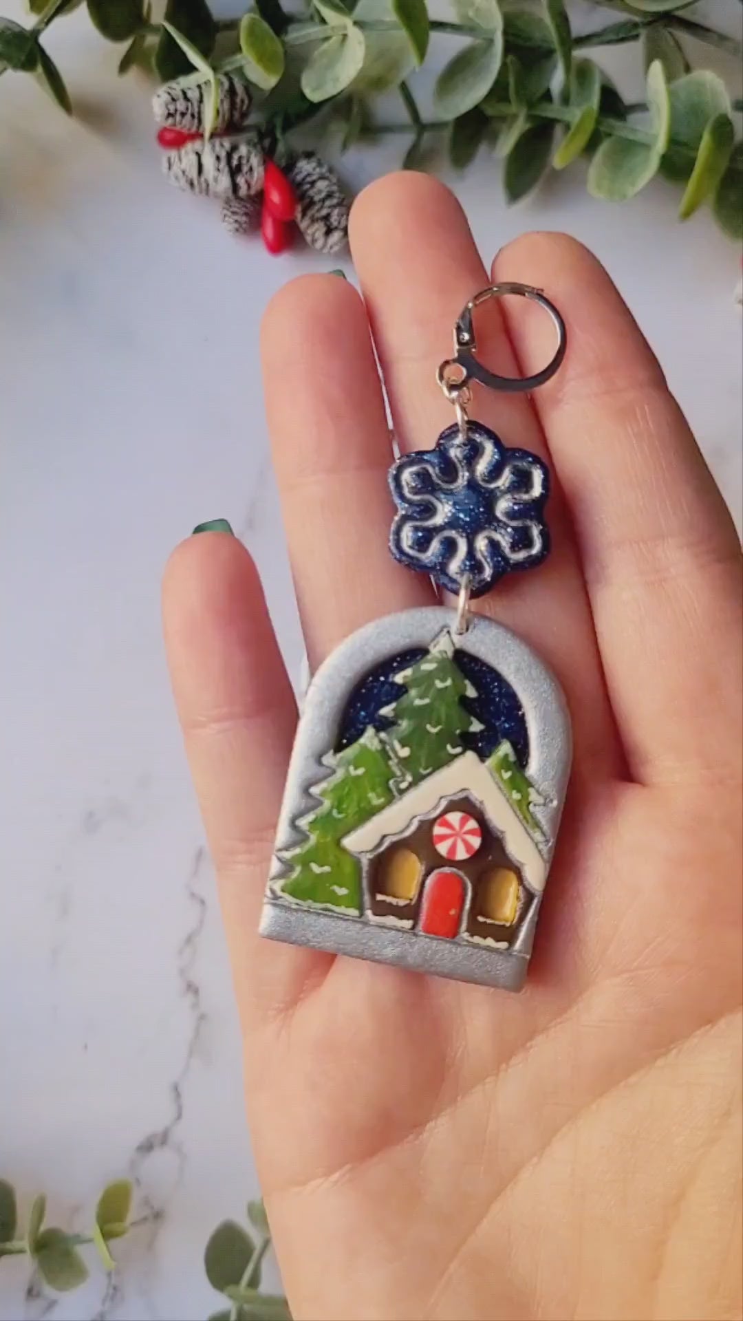 video close up of painted winter landscape earrings on a marble background with foliage. 